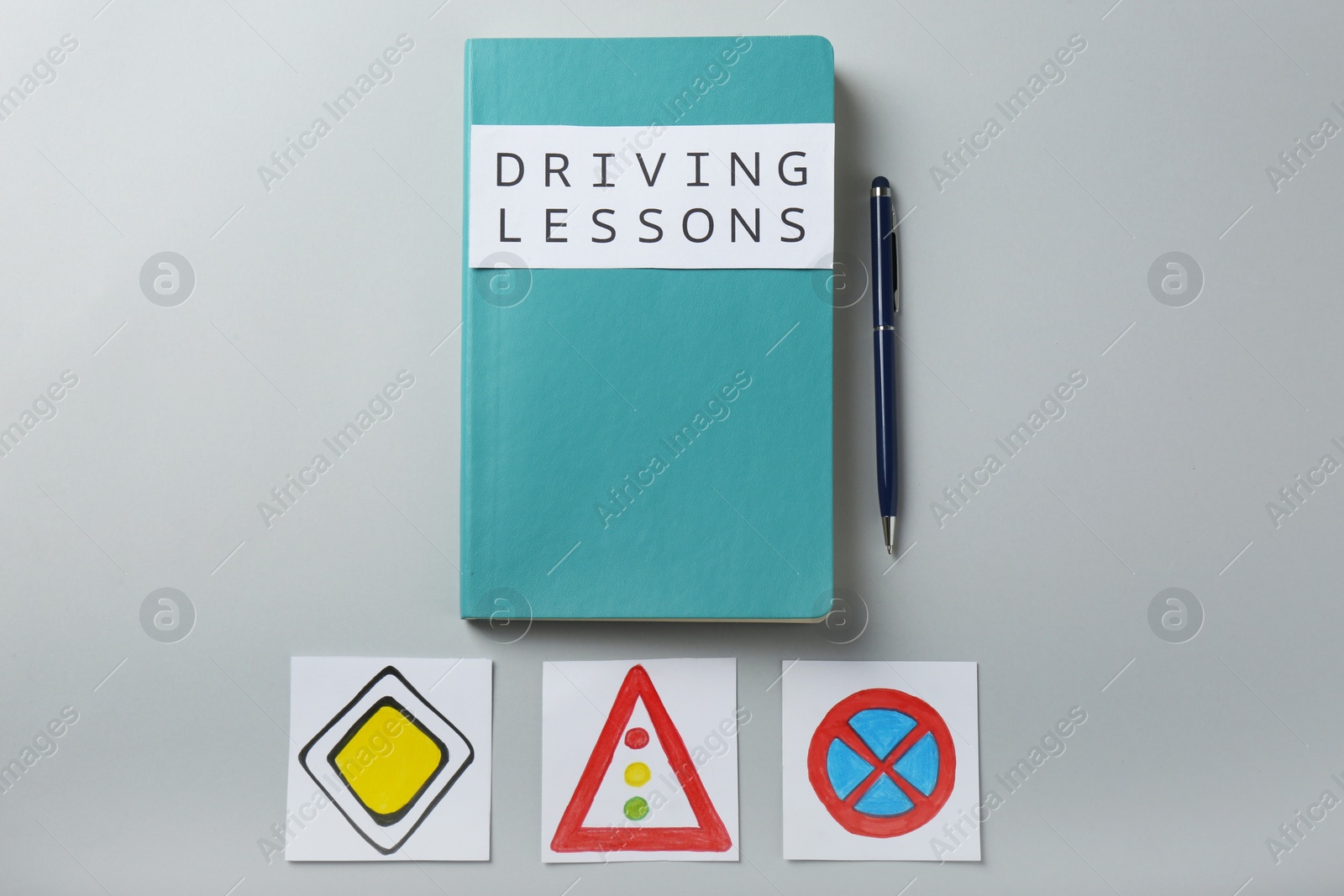 Photo of Flat lay composition with workbook for driving lessons and road signs on light grey background. Passing license exam
