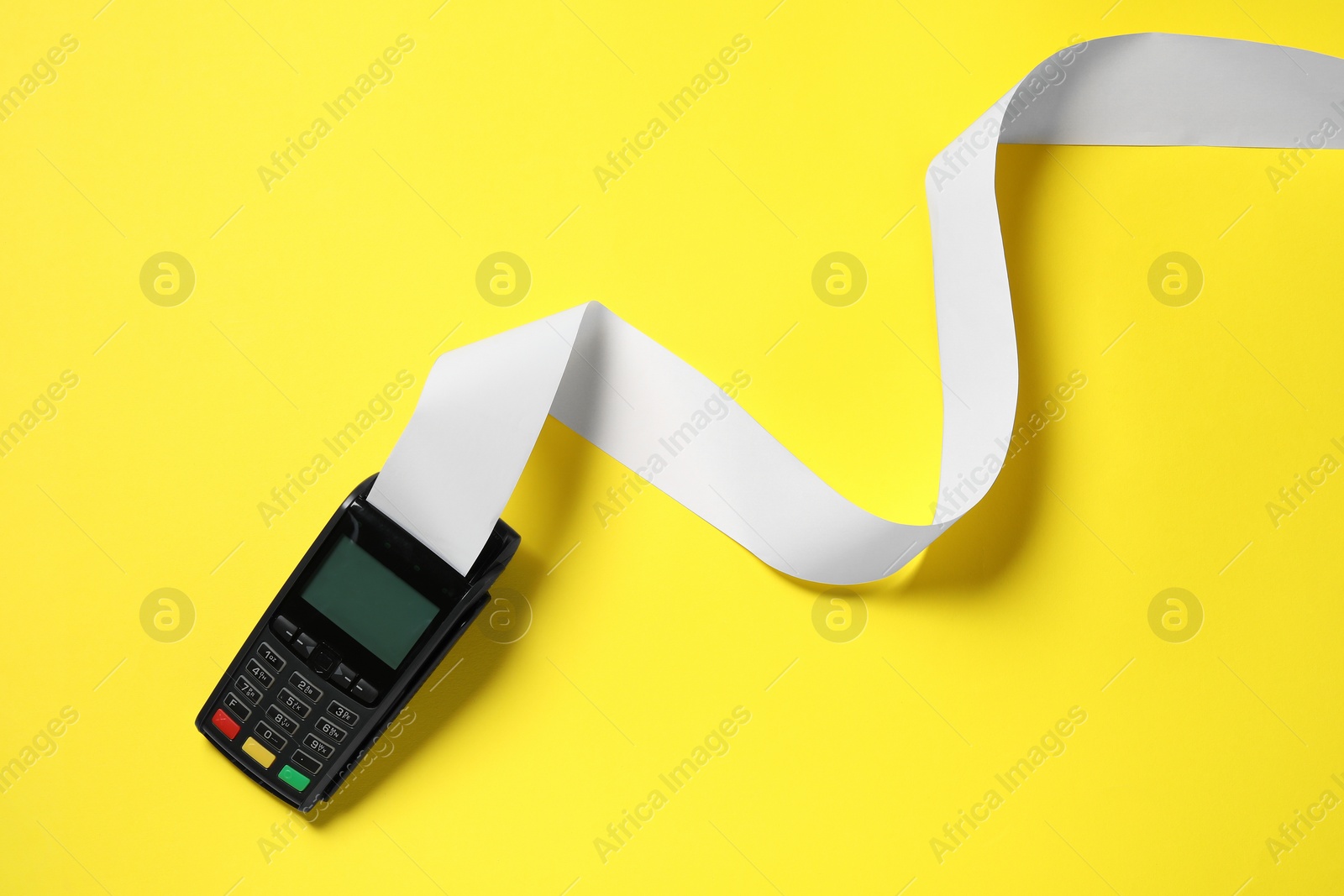 Photo of Payment terminal with thermal paper for receipt on yellow background, top view