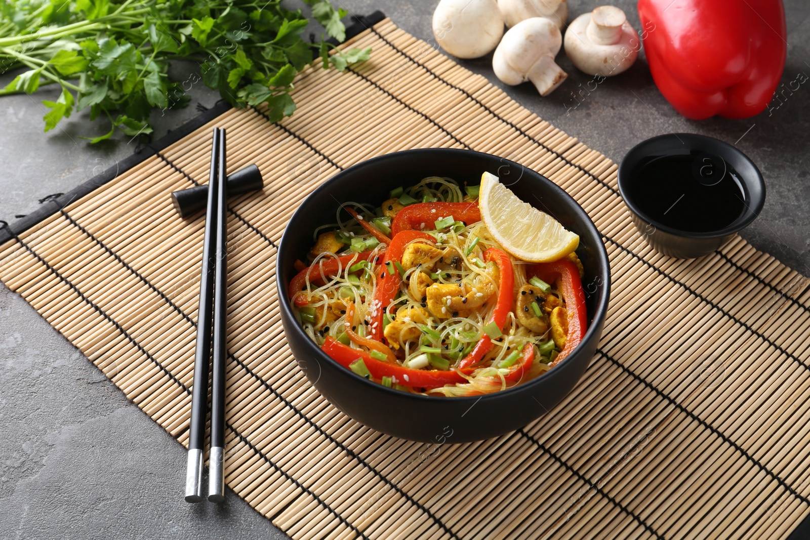 Photo of Stir-fry. Delicious cooked noodles with chicken and vegetables in bowl served on gray textured table