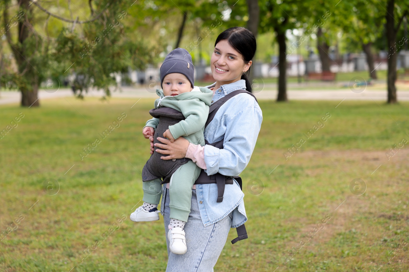 Photo of Mother holding her child in sling (baby carrier) in park