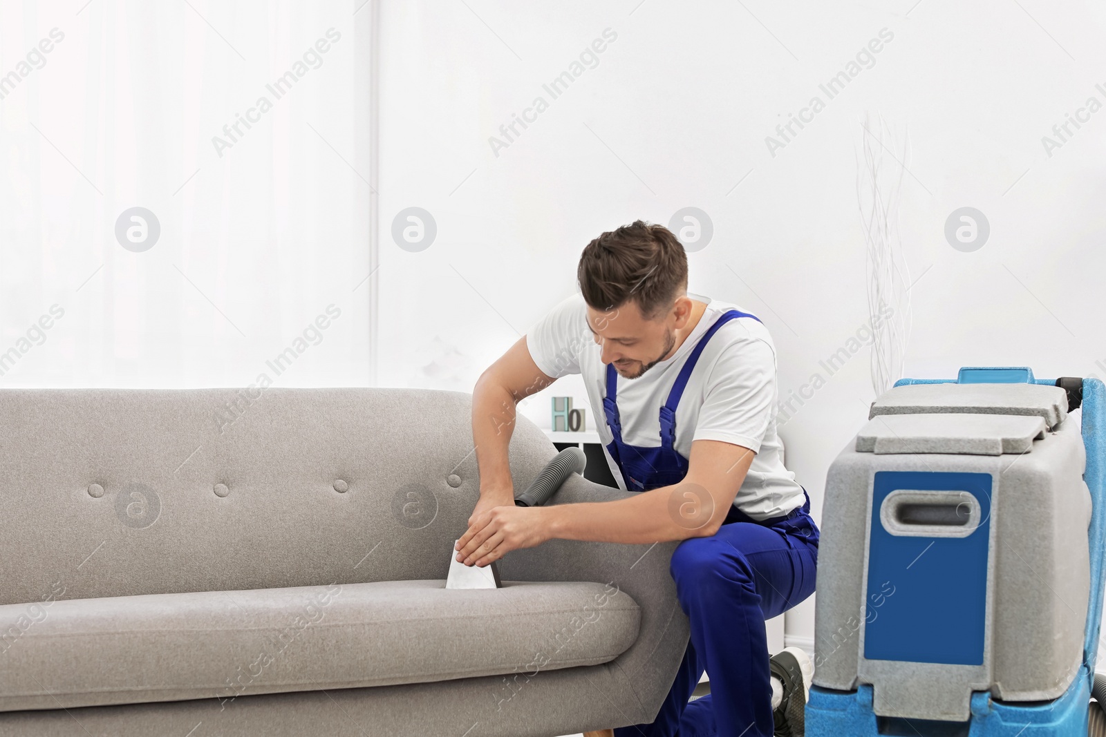 Photo of Dry cleaning worker removing dirt from sofa indoors