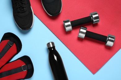 Photo of Exercise mat, dumbbells, bottle of water, weights and shoes on light blue background, flat lay