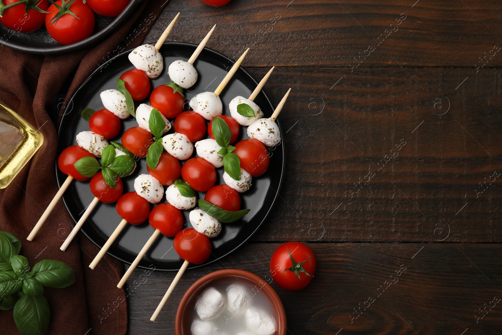 Photo of Caprese skewers with tomatoes, mozzarella balls, basil and spices on wooden table, flat lay. Space for text