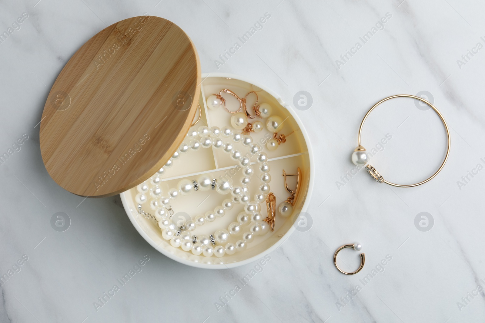 Photo of Stylish jewelry with pearls in box on white marble table, flat lay