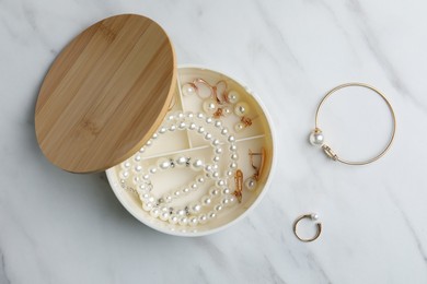 Stylish jewelry with pearls in box on white marble table, flat lay