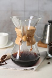 Photo of Glass chemex coffeemaker with tasty drip coffee and beans on white table