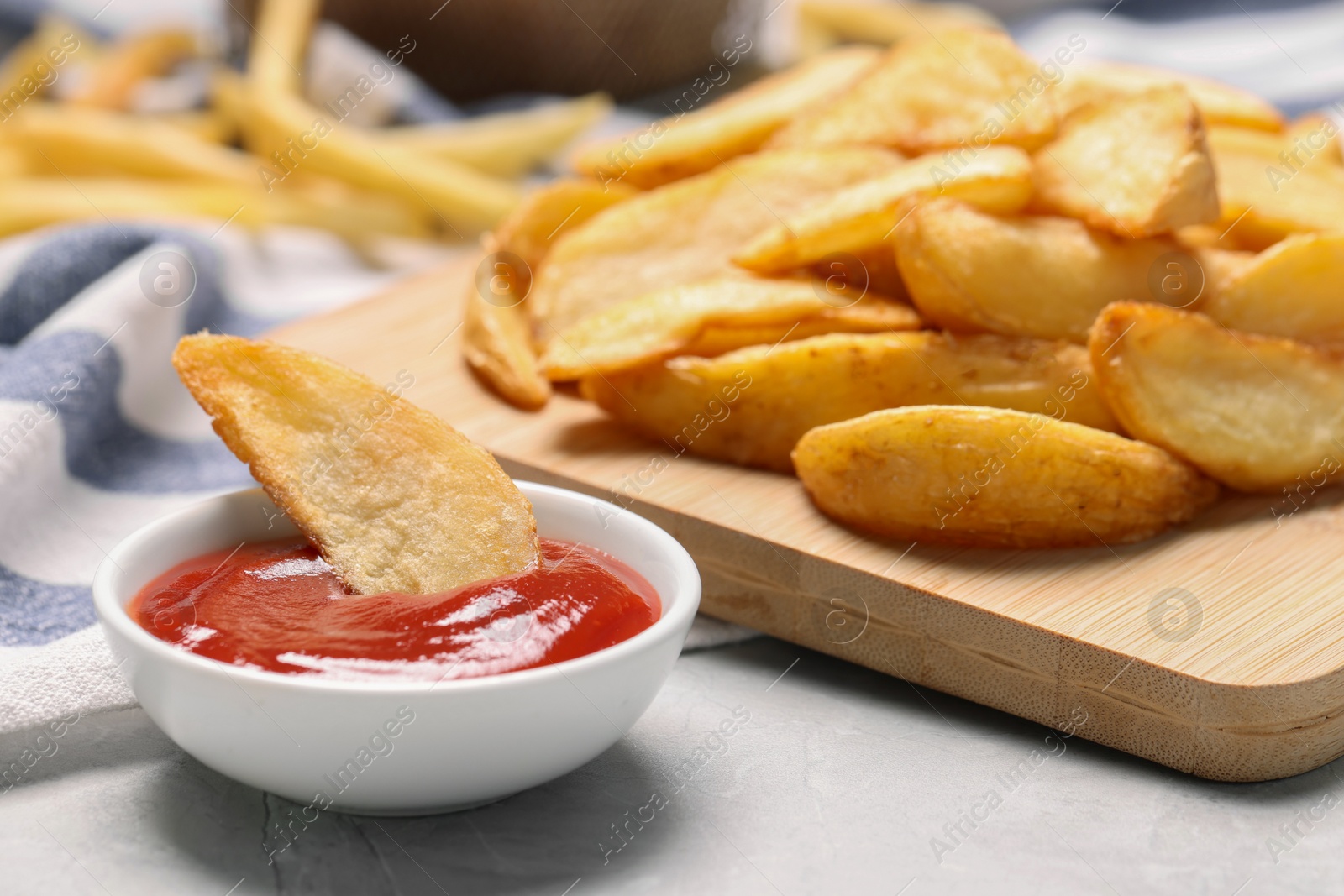 Photo of Delicious baked potato wedges and ketchup in bowl on light gray table, closeup