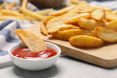 Delicious baked potato wedges and ketchup in bowl on light gray table, closeup