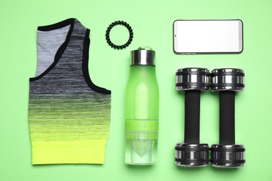 Photo of Flat lay composition with sports items and mobile phone on green background