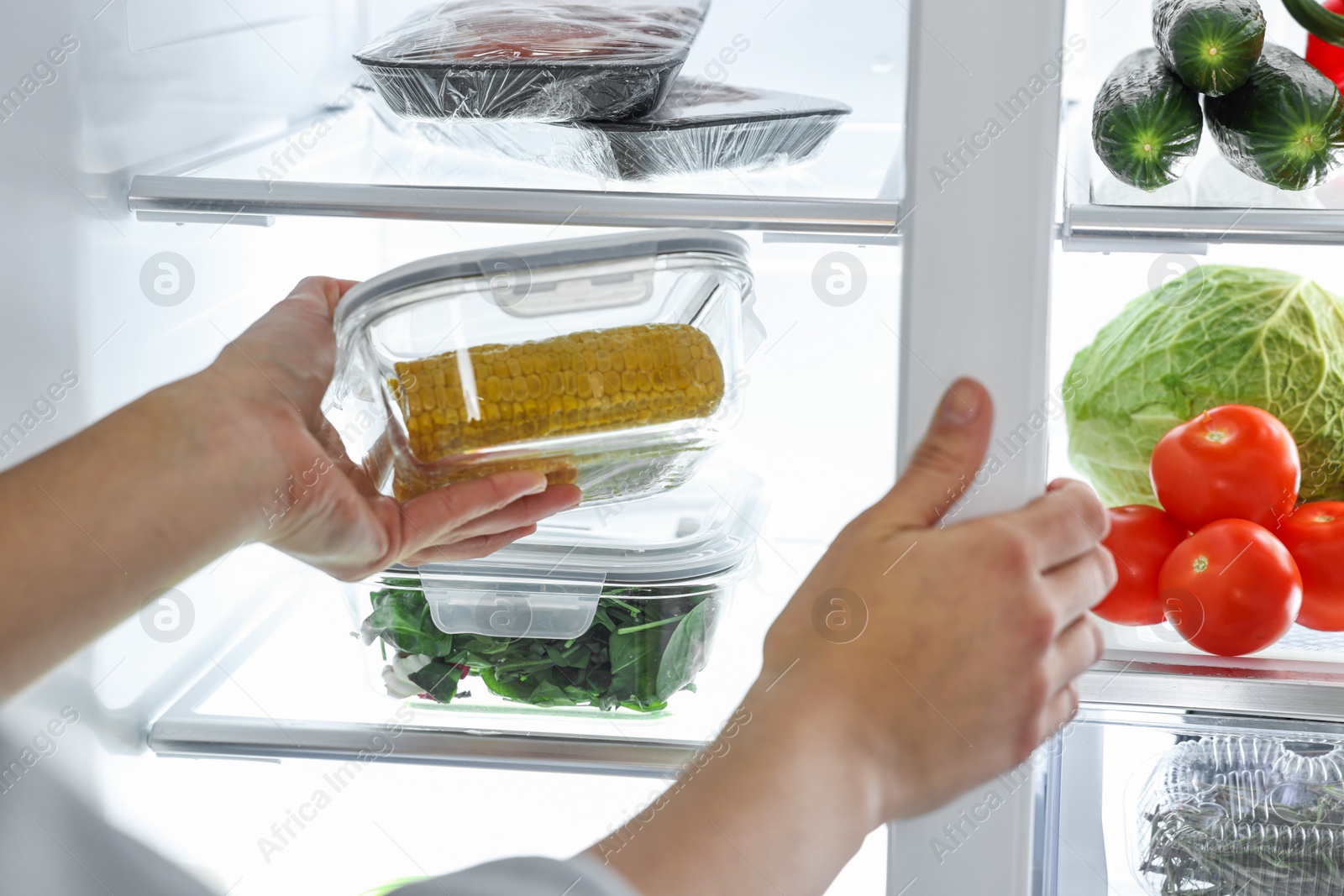 Photo of Young woman taking container with corn out of refrigerator, closeup