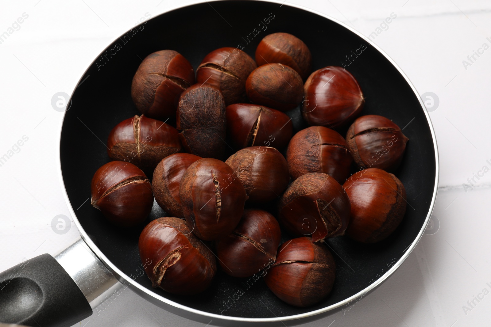 Photo of Fresh edible sweet chestnuts in frying pan on white tiled table, closeup