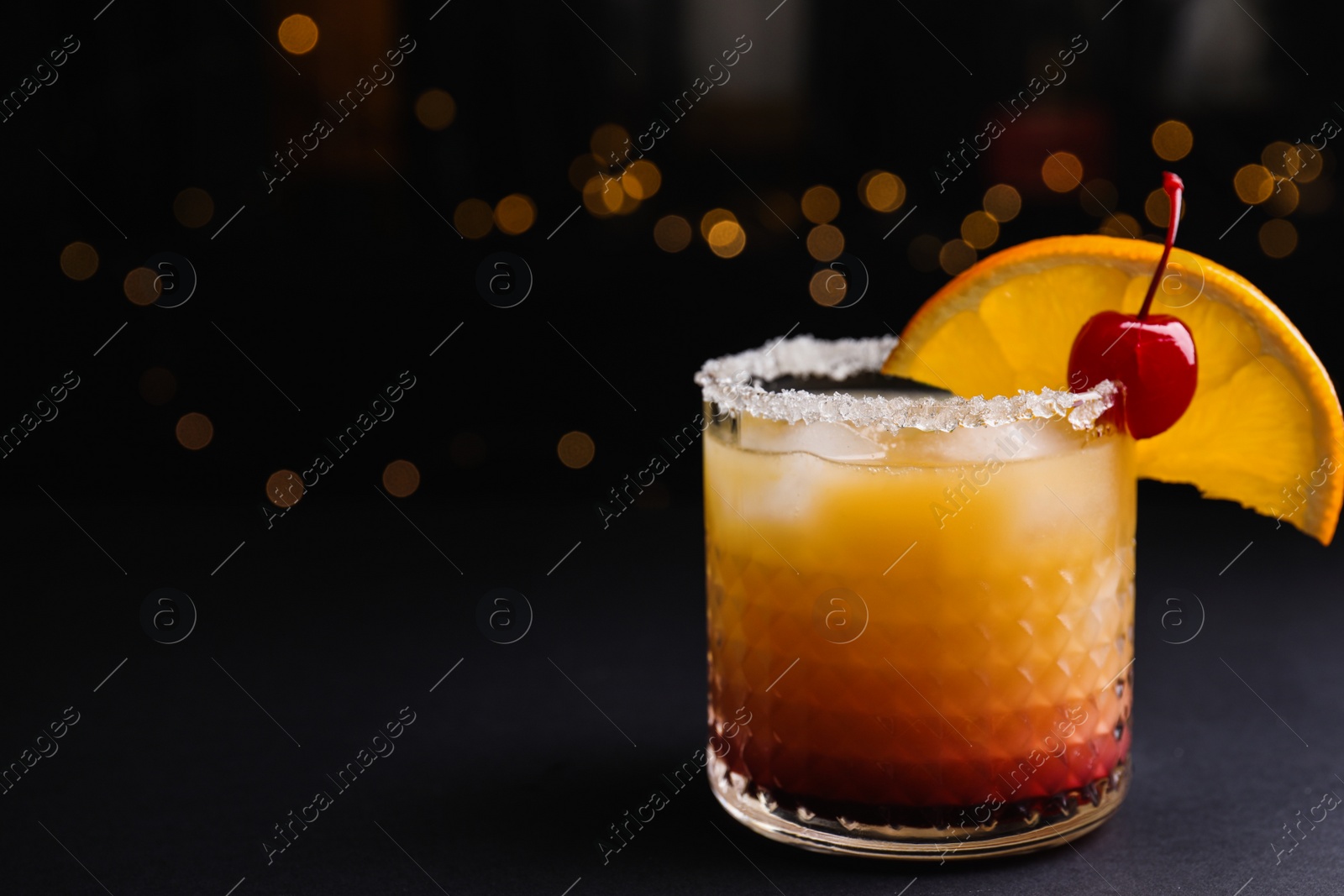 Photo of Fresh alcoholic Tequila Sunrise cocktail on black table. Space for text