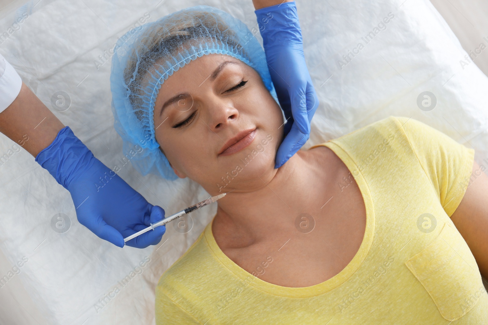 Photo of Mature woman with double chin receiving injection in clinic, above view