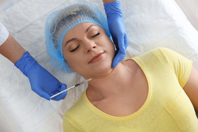 Mature woman with double chin receiving injection in clinic, above view