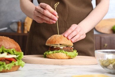 Photo of Woman making delicious vegetarian burger at white marble table, closeup