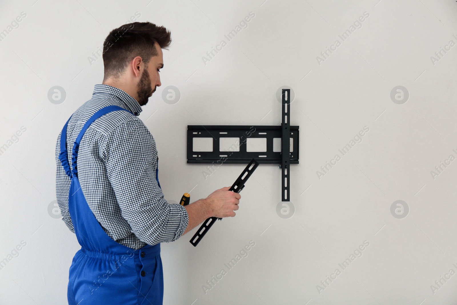 Photo of Professional technician installing TV bracket on wall indoors