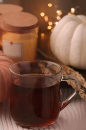 Photo of Cup of hot drink, candle and pumpkin on white knitted blanket indoors