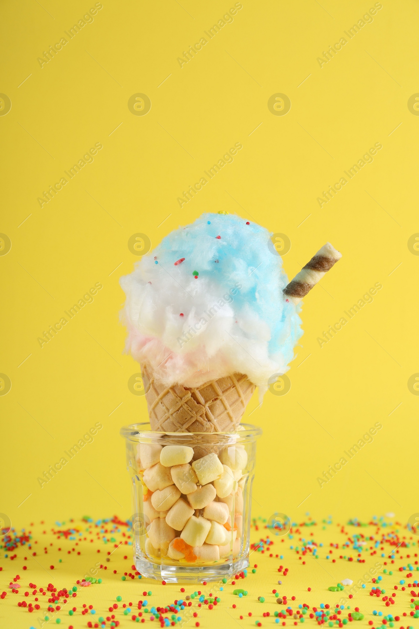 Photo of Sweet cotton candy in waffle cone on yellow background