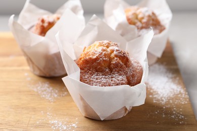 Photo of Delicious muffins with powdered sugar on wooden board, closeup