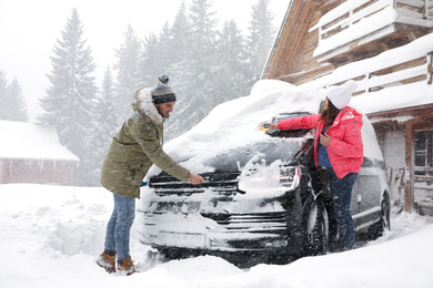 Young couple cleaning snow from car outdoors on winter day