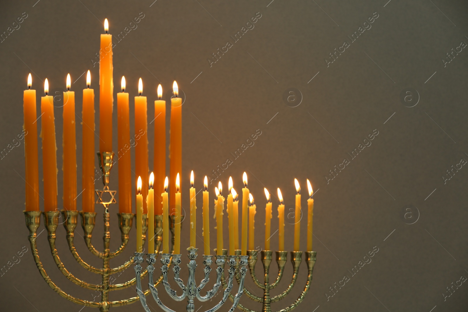 Photo of Hanukkah celebration. Menorahs with burning candles on light background, space for text