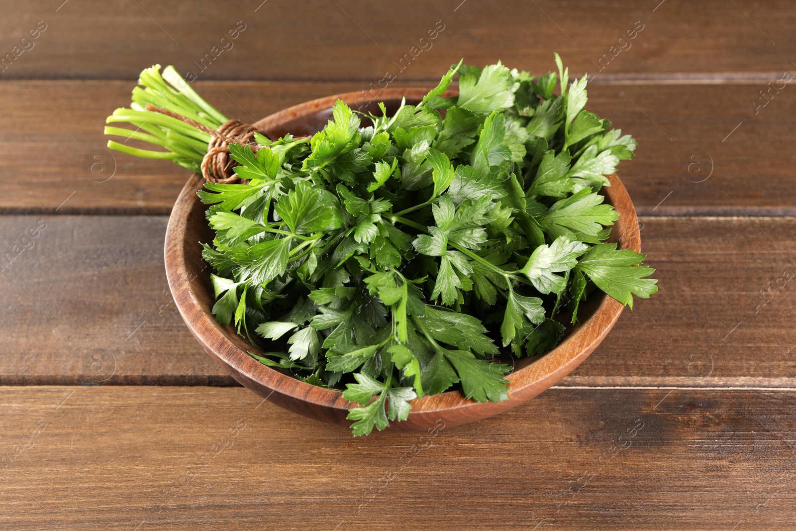 Photo of Bunch of fresh parsley in bowl on wooden table