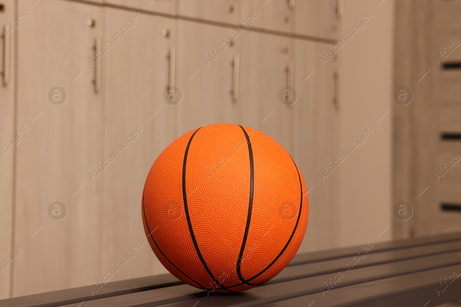 Photo of Orange basketball ball on wooden bench in locker room