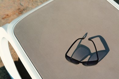 Stylish sunglasses on grey sunbed outdoors. Beach accessory, above view