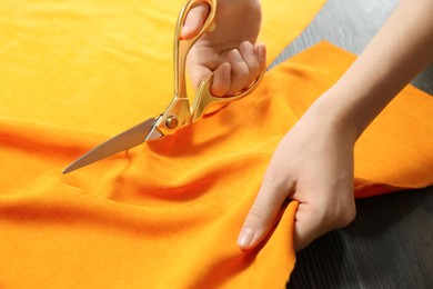 Seamstress cutting orange fabric with scissors at workplace, closeup