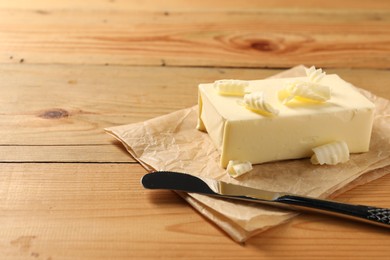 Photo of Tasty butter and knife on wooden table. Space for text