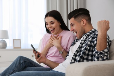 Photo of Emotional couple participating in online auction using smartphone at home
