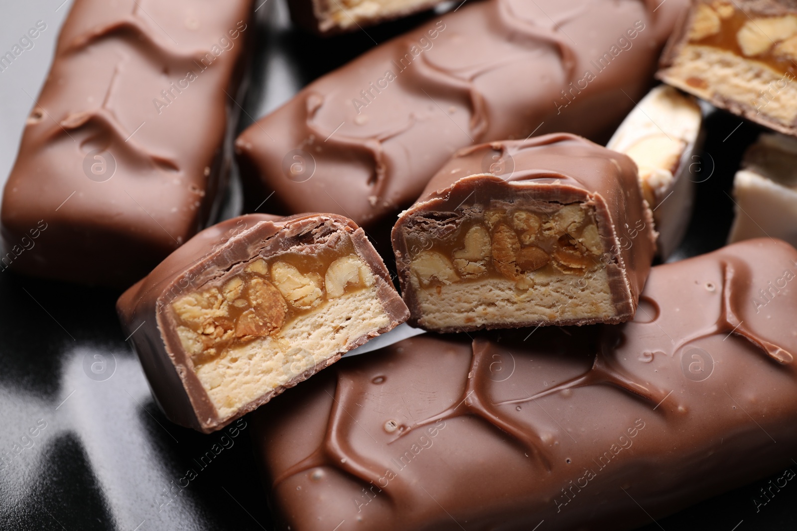 Photo of Tasty chocolate bars with nougat and nuts on black plate, closeup