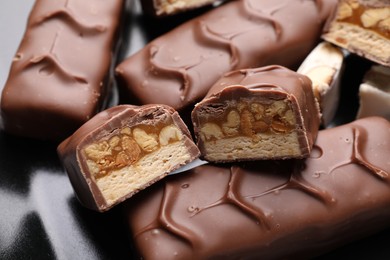 Photo of Tasty chocolate bars with nougat and nuts on black plate, closeup