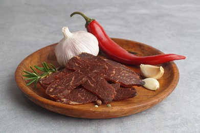 Photo of Plate with pieces of delicious beef jerky and spices on light grey table