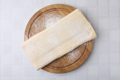 Photo of Raw puff pastry dough on white tiled table, top view