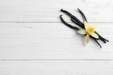 Flat lay composition with vanilla sticks and flower on wooden background. Space for text