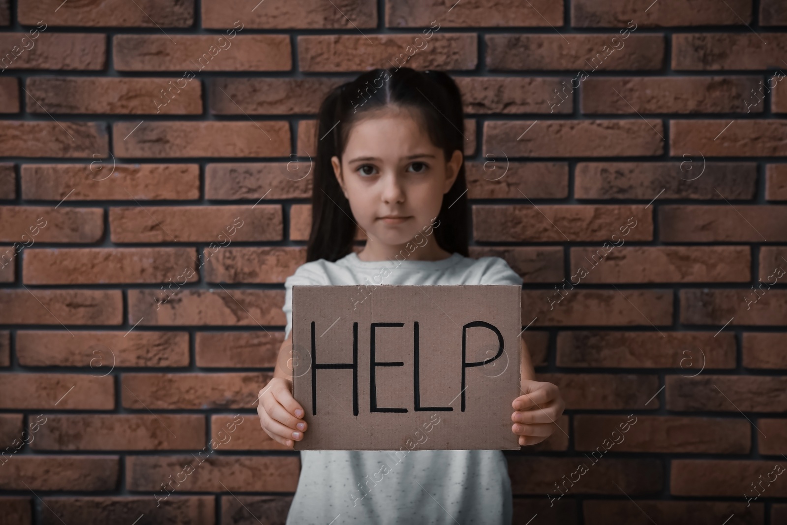 Photo of Sad little girl with sign HELP near brick wall. Child in danger