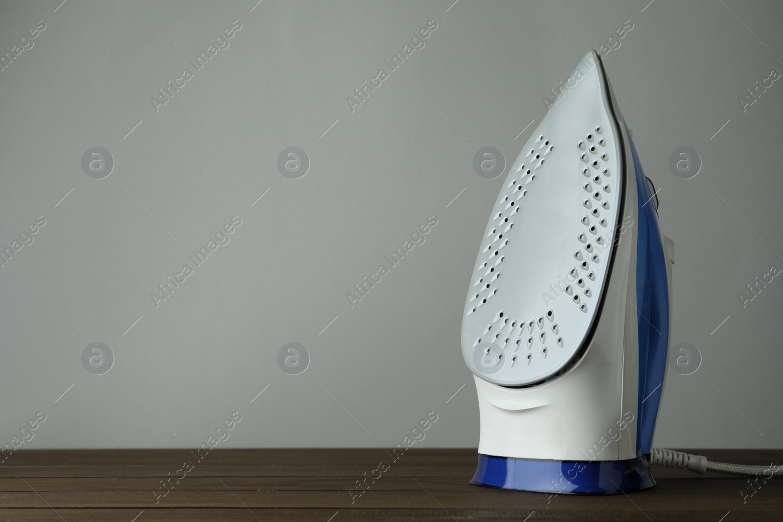 Photo of One modern iron on wooden table against light grey background, space for text. Home appliance