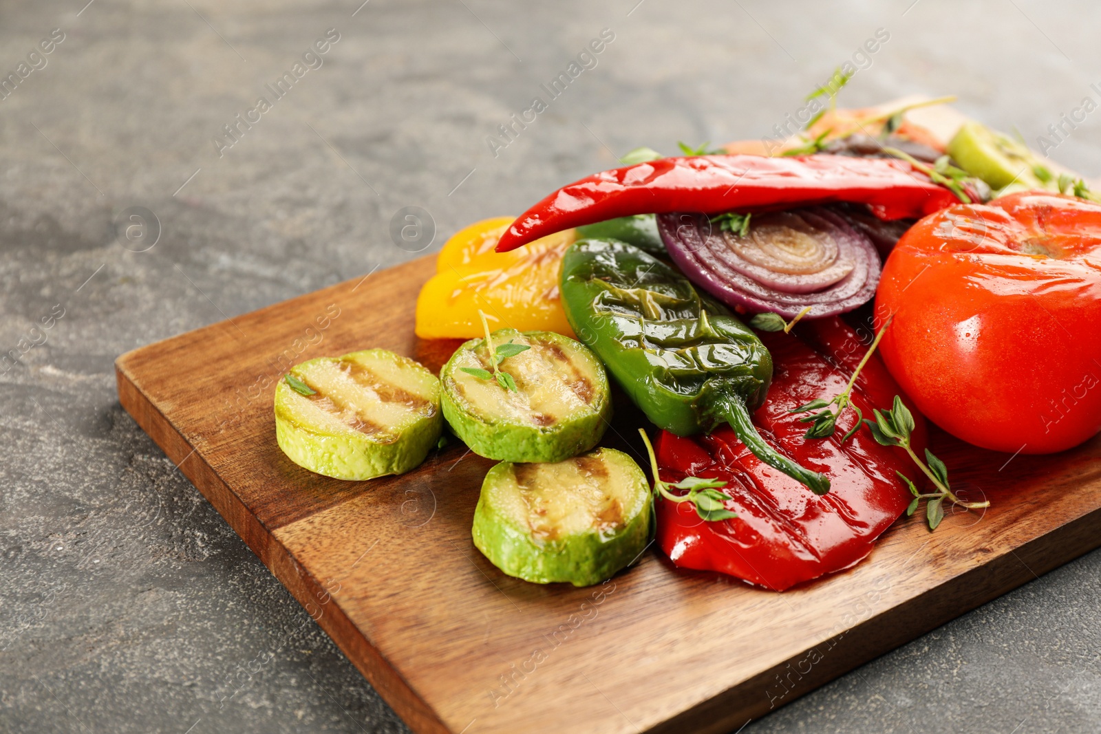 Photo of Wooden board with delicious grilled vegetables on grey table, closeup