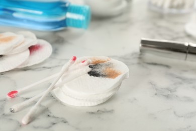 Photo of Dirty cotton pads, swabs and makeup removal product on white marble table, closeup