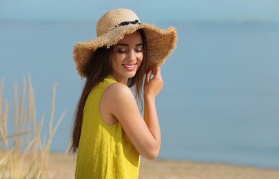 Photo of Beautiful young woman wearing straw hat on beach. Stylish headdress