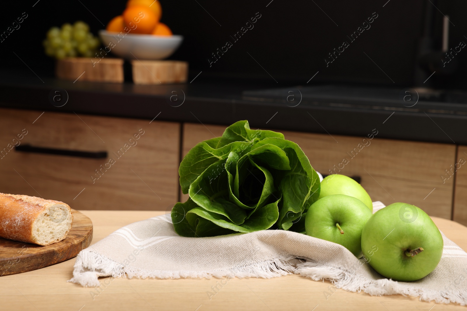 Photo of Ripe bok choy, green apples and baguette on table in kitchen