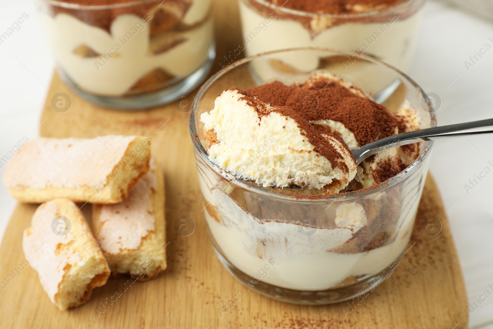 Photo of Delicious tiramisu in glasses, cookies and spoon on white table, closeup