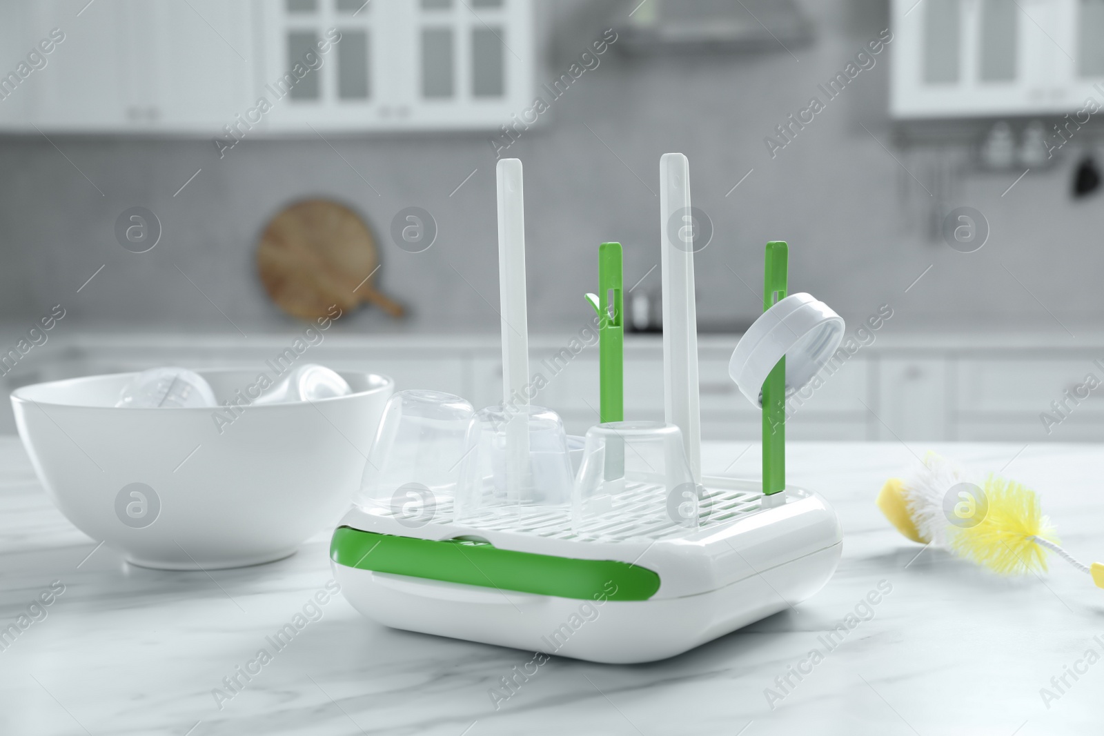 Photo of Dryer and bowl with baby bottle caps on white marble table in kitchen