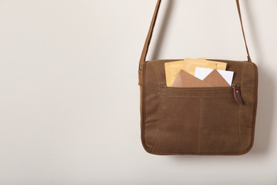 Photo of Brown postman bag with mails hanging on light wall, space for text
