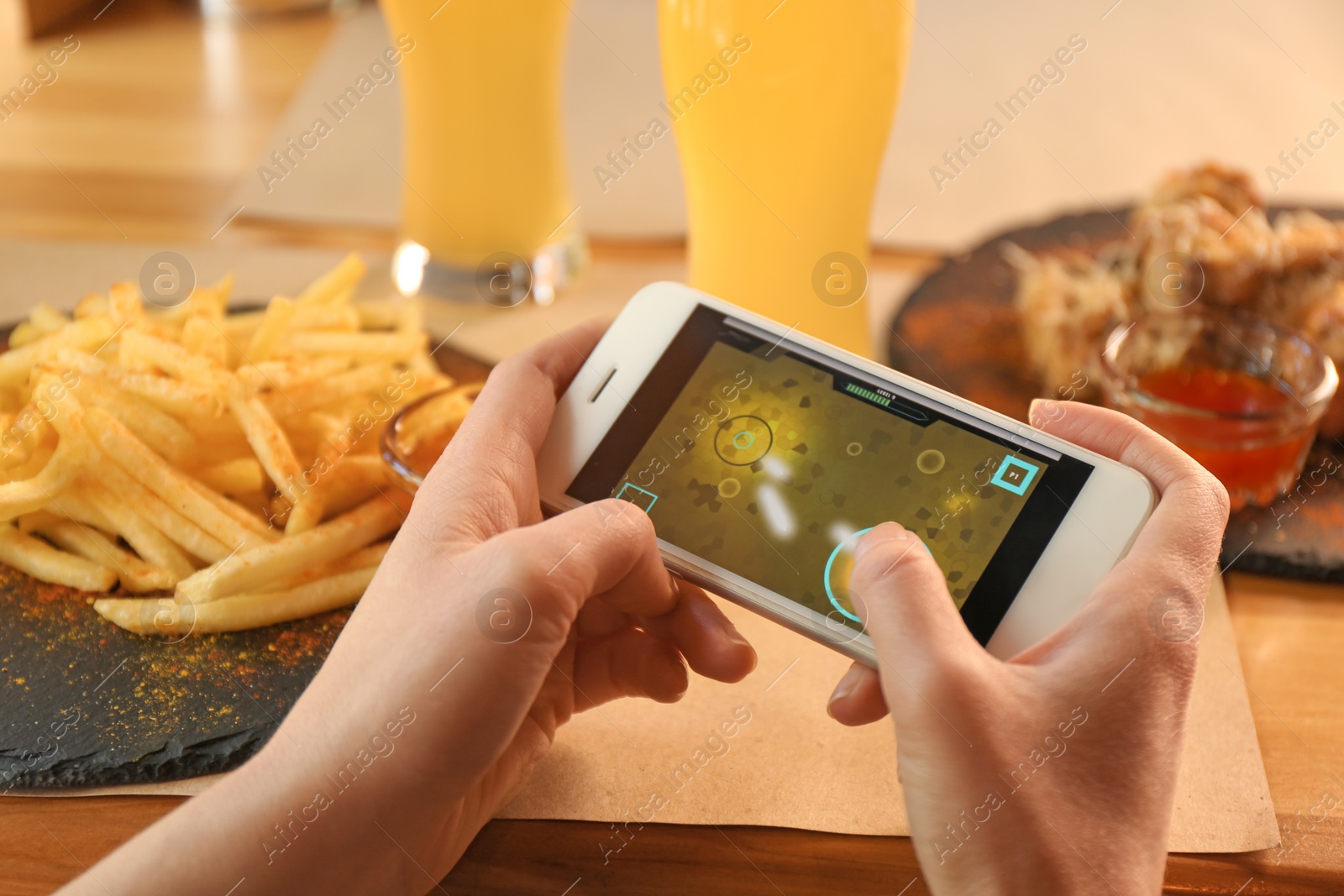 Photo of Woman playing game using smartphone at table with tasty snacks, closeup