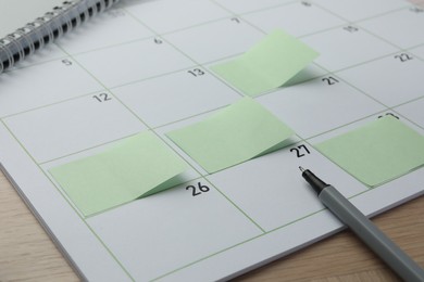 Photo of Timetable. Calendar page with green sticky notes and pen on wooden table, closeup