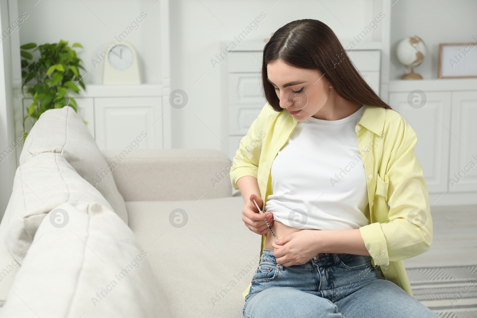 Photo of Diabetes. Woman making insulin injection into her belly on sofa at home, space for text