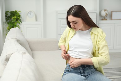 Diabetes. Woman making insulin injection into her belly on sofa at home, space for text