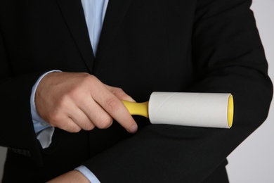 Man cleaning black jacket with lint roller on light grey background, closeup